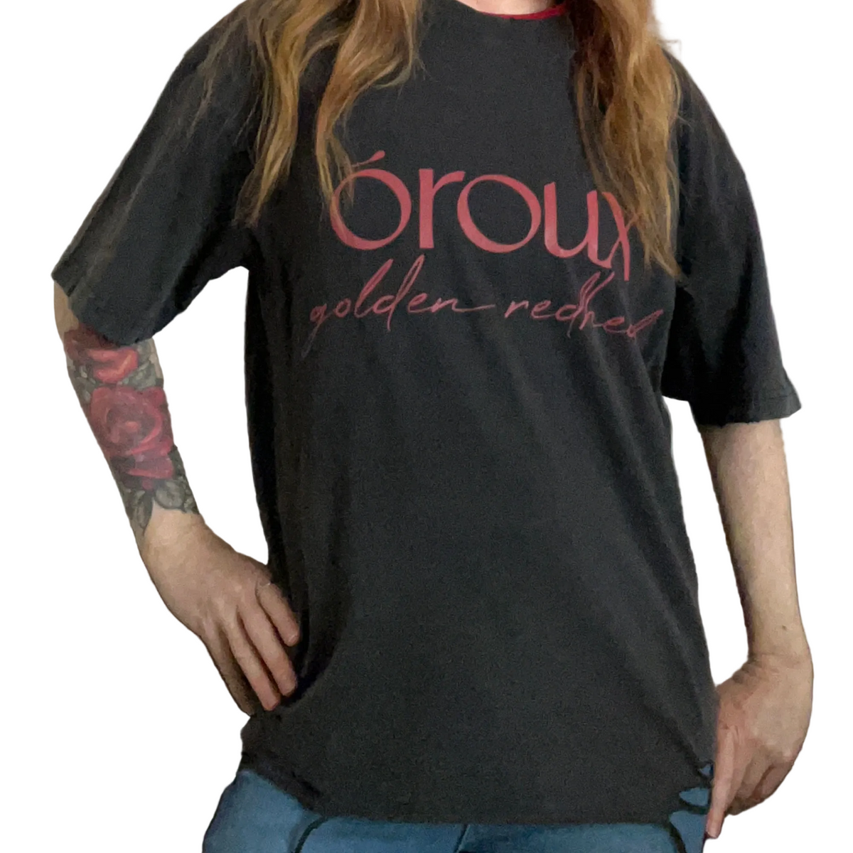A person wearing a faded black graphic t-shirt with 'órou golden red' printed in red script across the chest, paired with blue jeans.