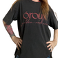 A person wearing an oversized black graphic T-shirt with pink text reading 'oroux golden redhead' across the front, standing indoors with hands on hips.
