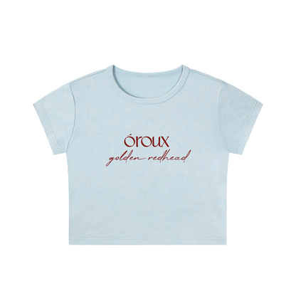 A light blue short-sleeve crop top t-shirt with 'oroux golden redhead' printed in red on the chest, shown against a plain white background.