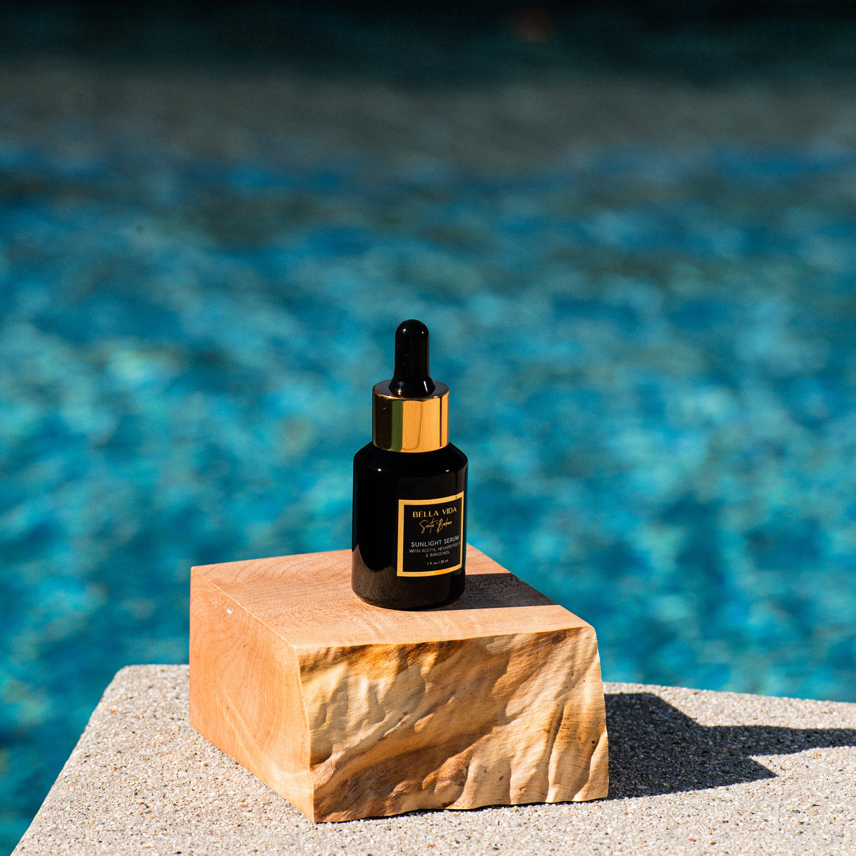 black Bella Vida Santa Barbara luxury skincare bottles with gold caps . Sunlight Serum, by pool