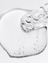 A close-up of a clear, transparent gel or adhesive patch with visible air bubbles and a glossy, flexible edge on a light gray background. texture of barrier balance jelly serum by oroux skin
