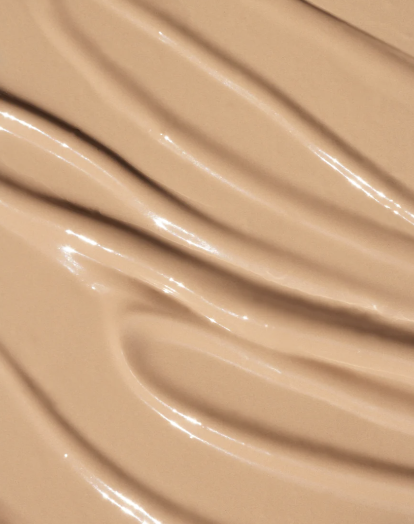 A close-up texture shot of a smooth, glossy beige liquid foundation or concealer swatch with elegant curved ridges. oroux skin