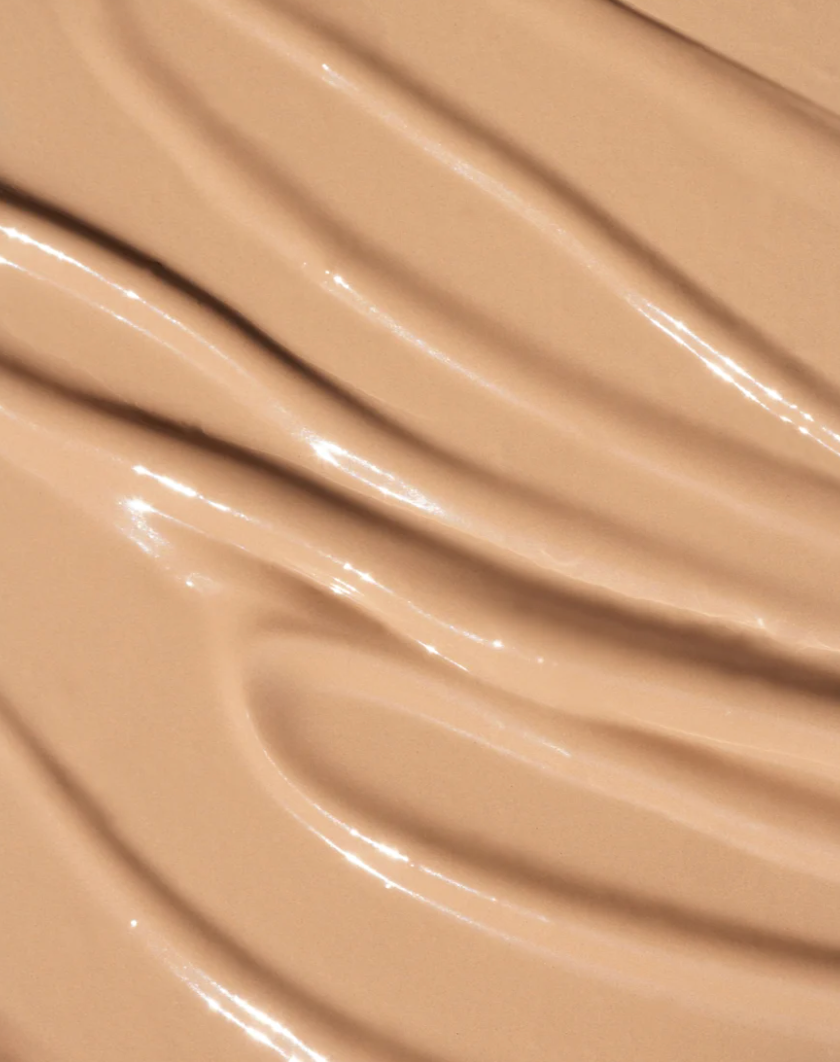 A close-up texture shot of a smooth, glossy beige liquid foundation or concealer swatch with elegant curved ridges. oroux skin