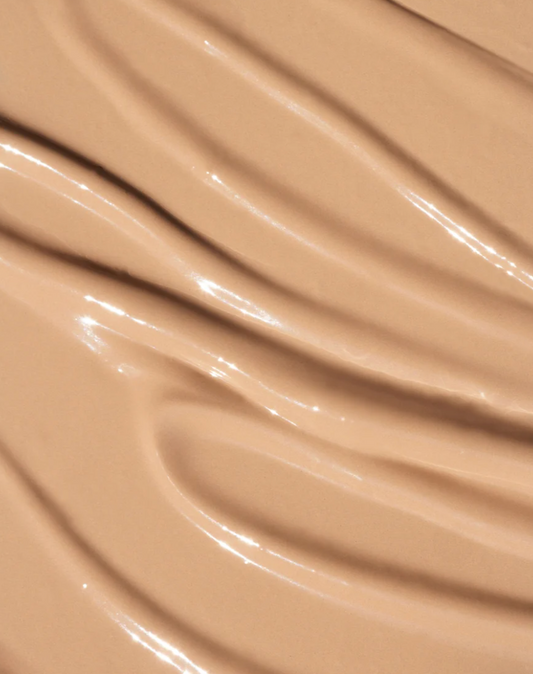 A close-up texture shot of a smooth, glossy beige liquid foundation or concealer swatch with elegant curved ridges. oroux skin