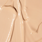 A close-up of a smooth, glossy beige cosmetic cream or foundation swatch with soft ridges and reflective highlights.