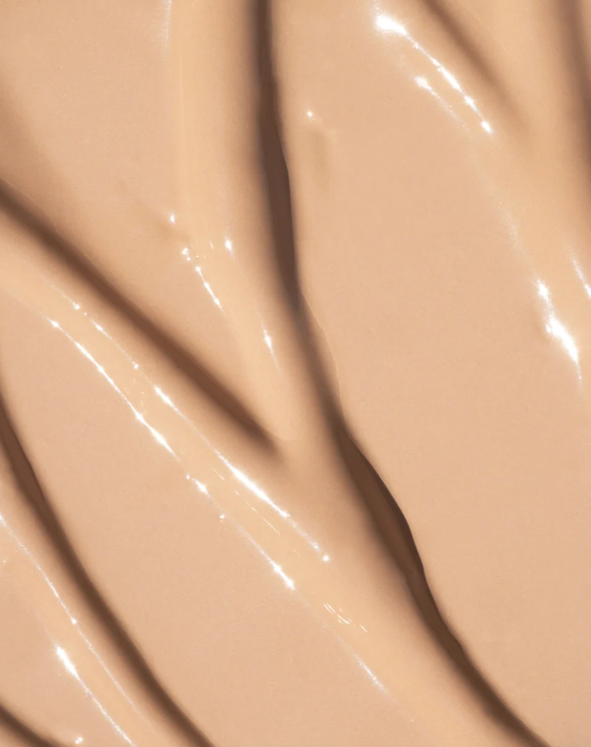 A close-up of a glossy, creamy beige cosmetic product swatch with smooth, swirled texture and soft highlights.