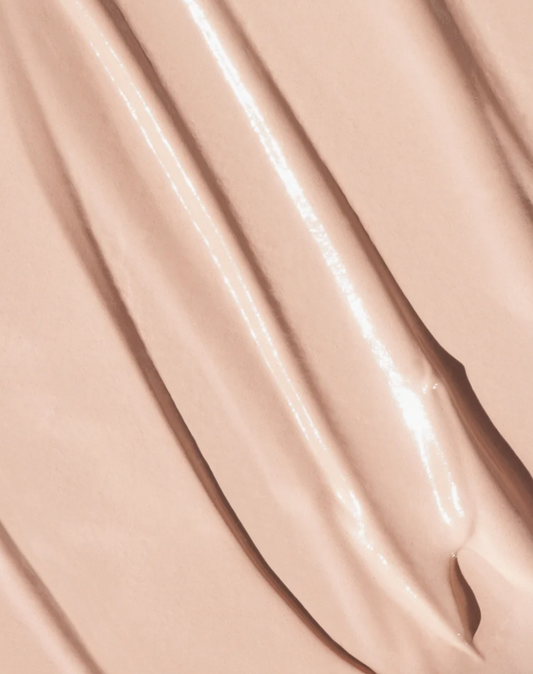 Close-up of a smooth, glossy beige cosmetic cream concealer by oroux skin or foundation swatch with diagonal ridges and soft highlights.