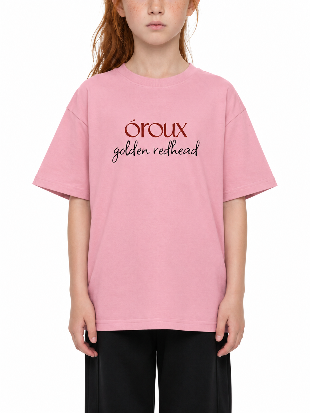 A child wearing an oversized light pink t-shirt with 'oroux golden redhead' printed on the chest, paired with black pants, against a plain white background.