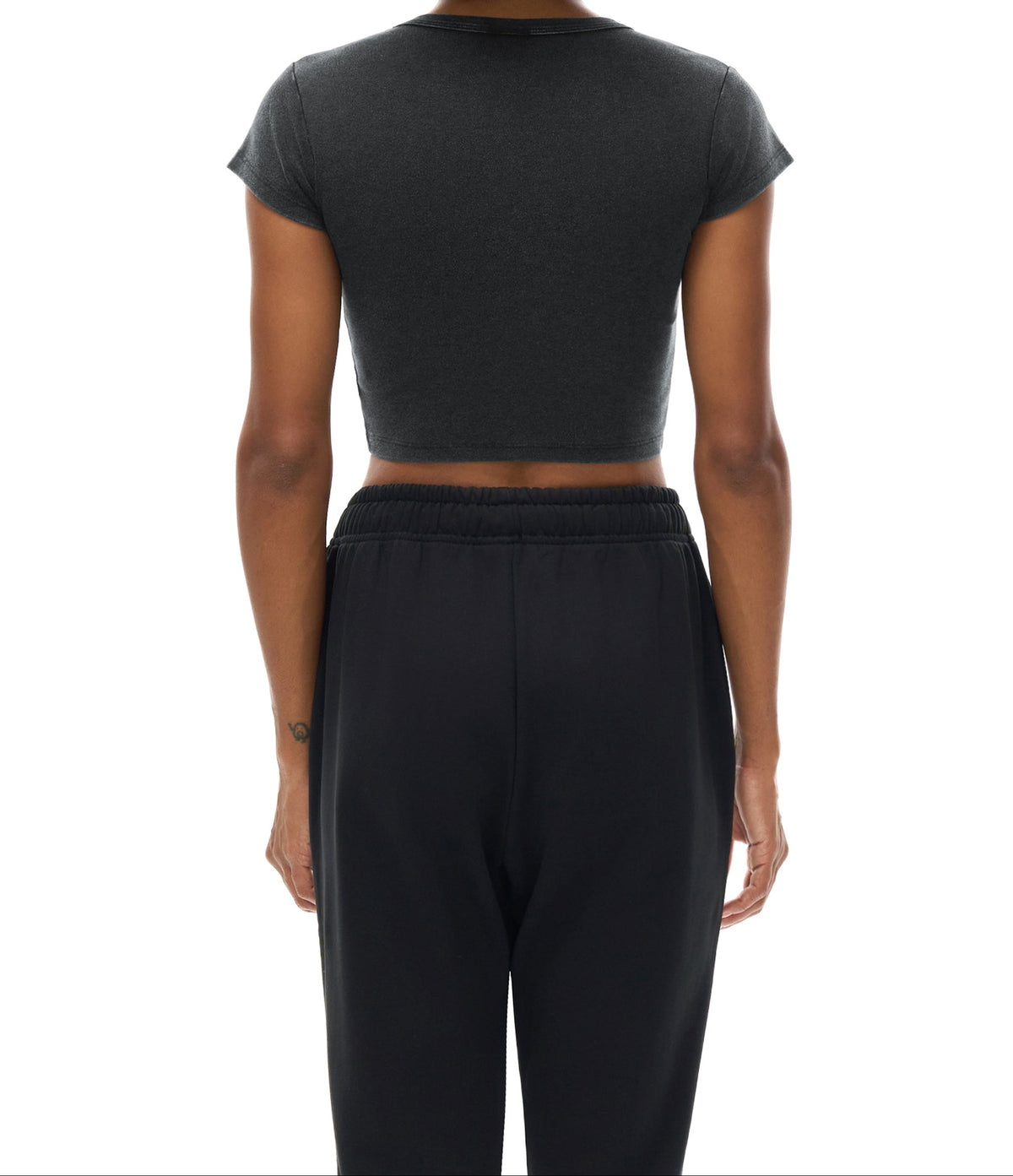 Person wearing a black crop top and black pants on a white background showing back of shirt