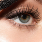 Close-up of a person's eye with long, curled, and voluminous black eyelashes, with a black mascara wand visible at the top left.