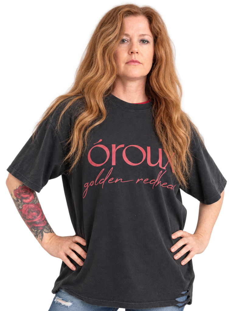 A side-by-side comparison of a woman wearing a black graphic t-shirt with pink text that reads 'oroux golden redhead'. The image shows the same model from the waist up, with the shirt displayed in two slightly different poses against a plain white background.