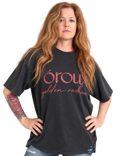 A side-by-side comparison of a woman wearing a black graphic t-shirt with pink text that reads 'oroux golden redhead'. The image shows the same model from the waist up, with the shirt displayed in two slightly different poses against a plain white background.