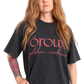 A side-by-side comparison of a woman wearing a black graphic t-shirt with pink text that reads 'oroux golden redhead'. The image shows the same model from the waist up, with the shirt displayed in two slightly different poses against a plain white background.