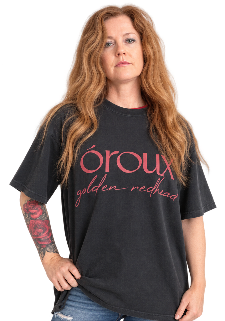 A side-by-side comparison of a woman wearing a black graphic t-shirt with pink text that reads 'oroux golden redhead'. The image shows the same model from the waist up, with the shirt displayed in two slightly different poses against a plain white background.
