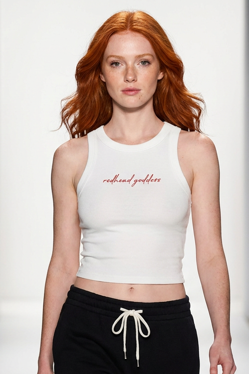 A model walks down a fashion runway wearing a white ribbed crop top with 'michael goldstein' printed in red script across the chest, paired with black sweatpants with a white drawstring.