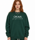 A woman with red hair wearing a dark green crewneck sweatshirt with white text that reads &