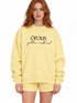 A woman with red hair wearing a pale yellow sweatshirt and matching shorts. The sweatshirt features the text &