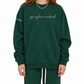 A model with red hair wearing a dark green crewneck sweatshirt with the phrase 'yes, my hair is natural' printed in white script across the chest, paired with matching green sweatpants against a plain white background.